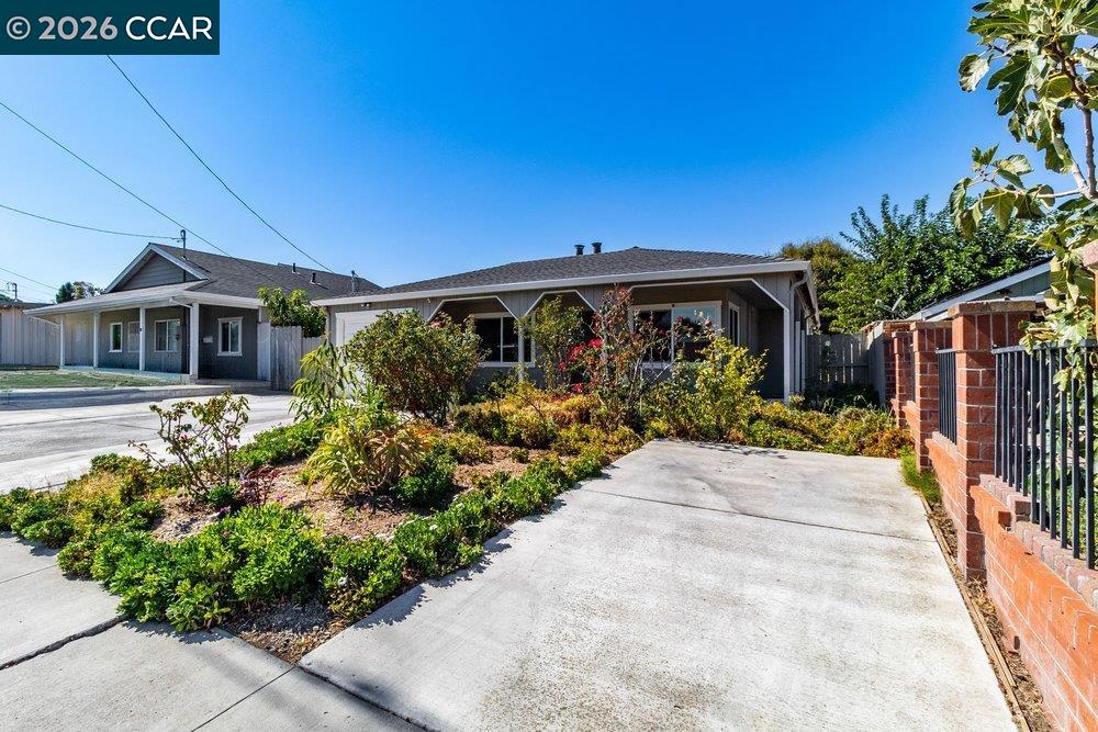 Single-story home with a broad concrete driveway, landscaped front garden, and brick-and-metal fence.