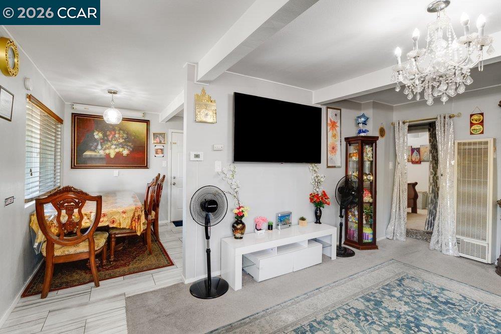 Living room and dining area with a wall-mounted TV, crystal chandelier, and carved wooden dining set.