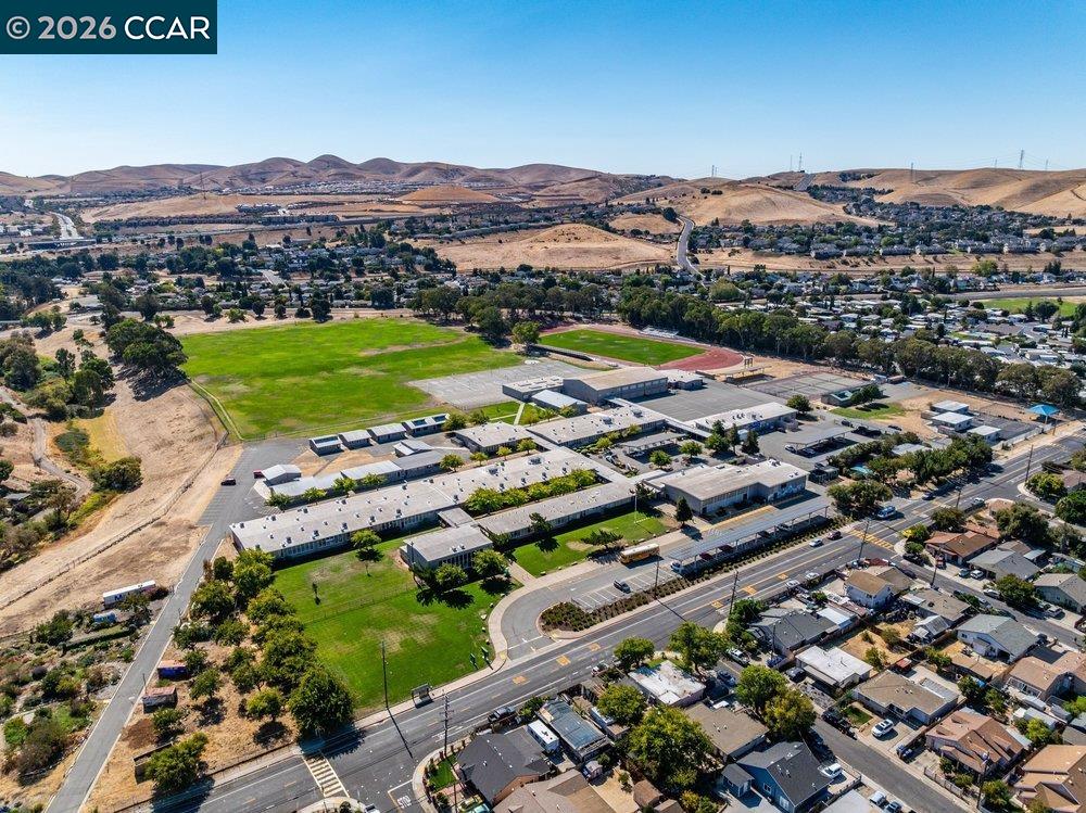 Aerial view of a school campus with green playing fields, nearby neighborhoods, and dry hills.