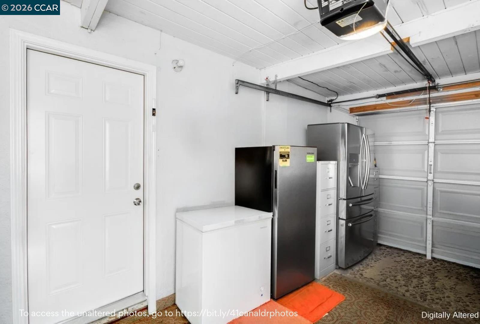 Garage with a chest freezer, stainless-steel refrigerator, and interior entry door.