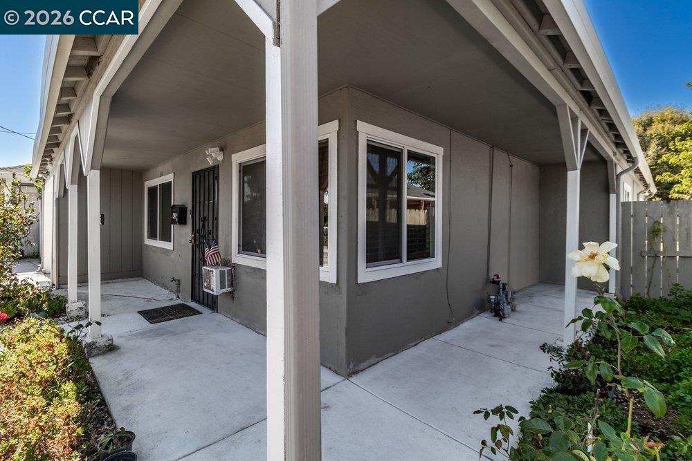 Gray house exterior with a covered entry, concrete walkway, white posts, and garden beds.