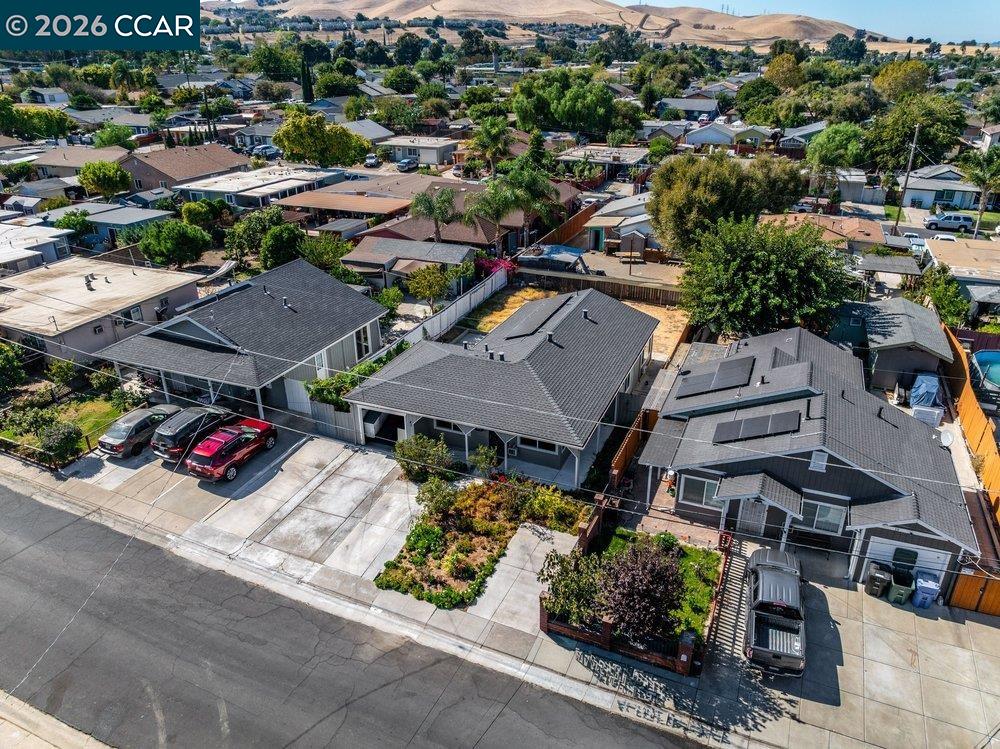 Aerial view of a gray-roofed home with a front garden and driveway among neighboring homes.