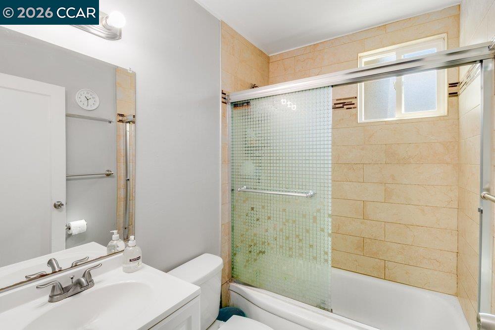 Bathroom with a beige-tiled tub and glass shower enclosure beside a white vanity.