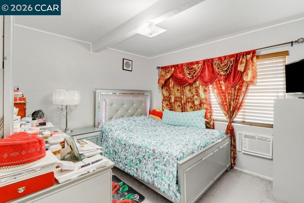 Bedroom with a silver bed, pale blue patterned bedding, ornate red curtains, and a window air conditioner.