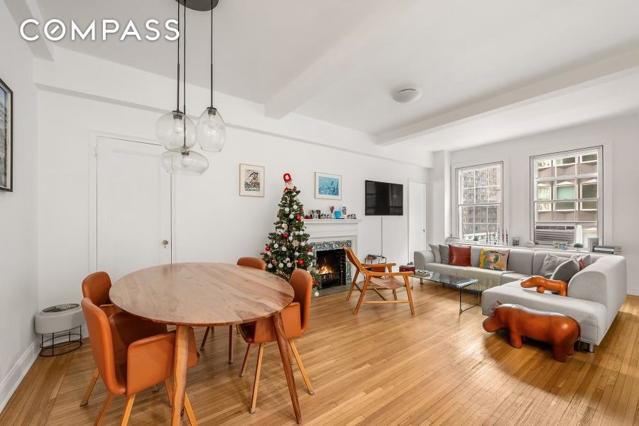 Living and dining room with hardwood floors, orange dining chairs, gray sofa, fireplace, and decorated Christmas tree.