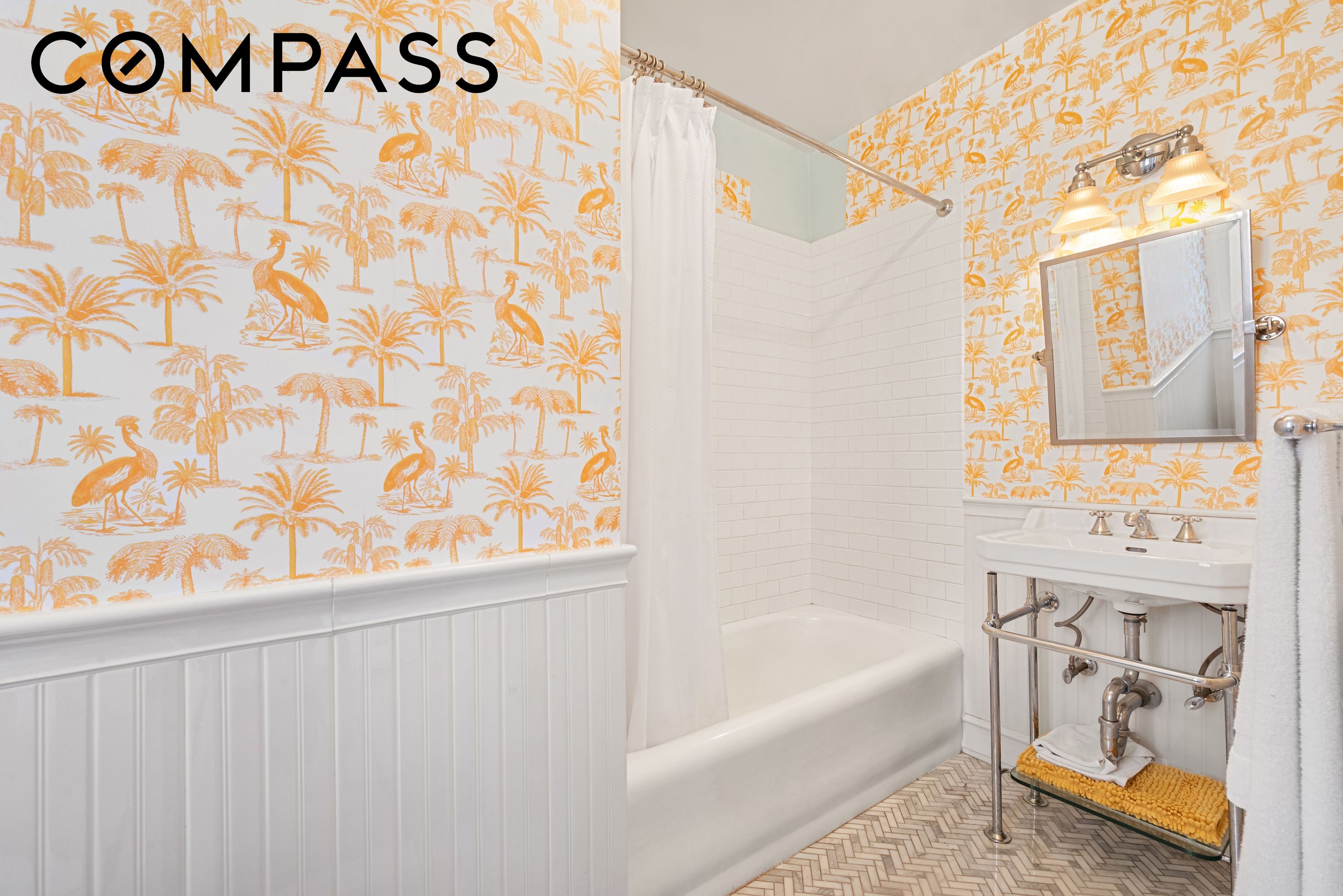 Bathroom with orange tropical wallpaper, white subway-tile tub surround, and a sink with exposed chrome plumbing.
