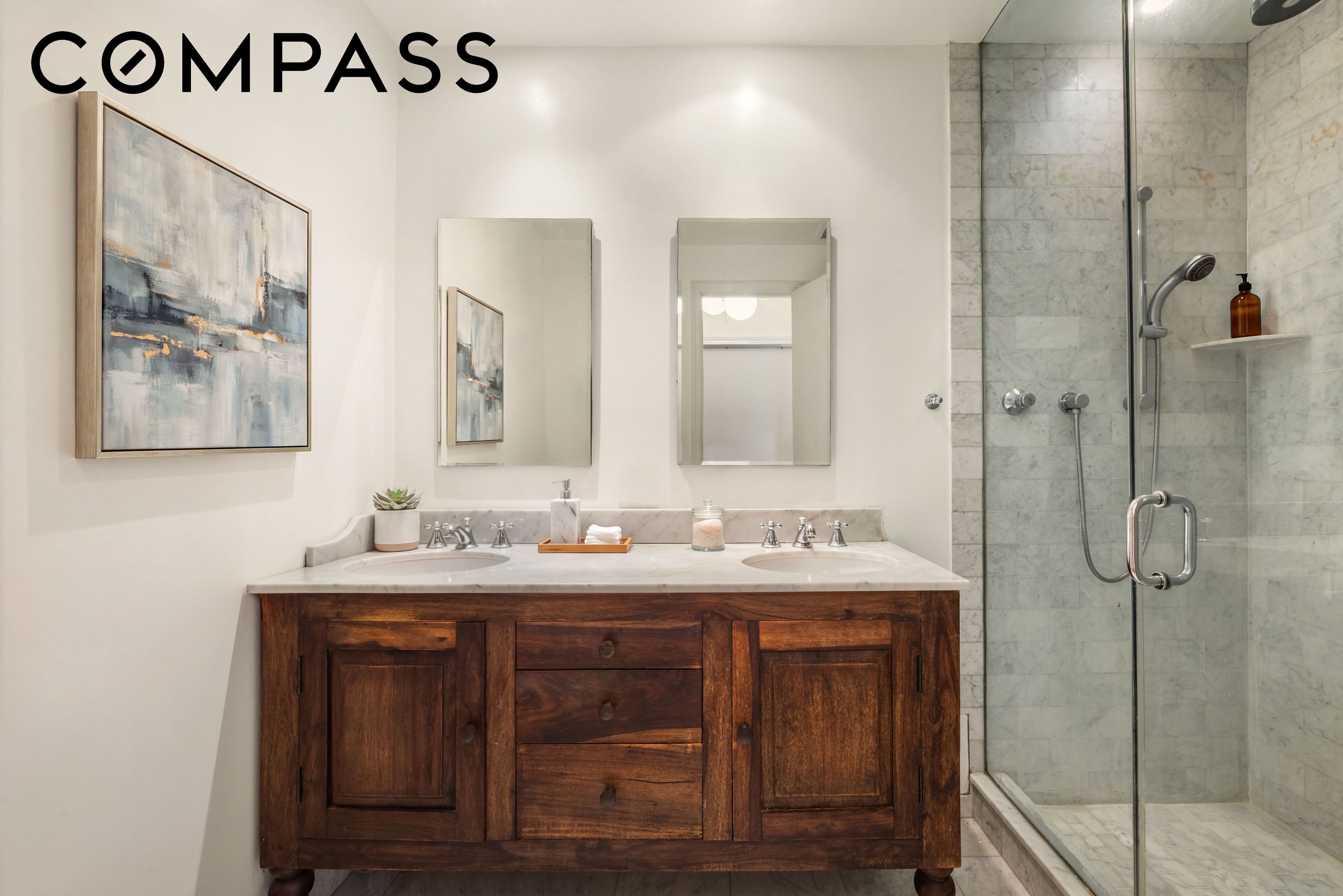Bathroom with a dark wood double vanity and glass-enclosed marble shower.