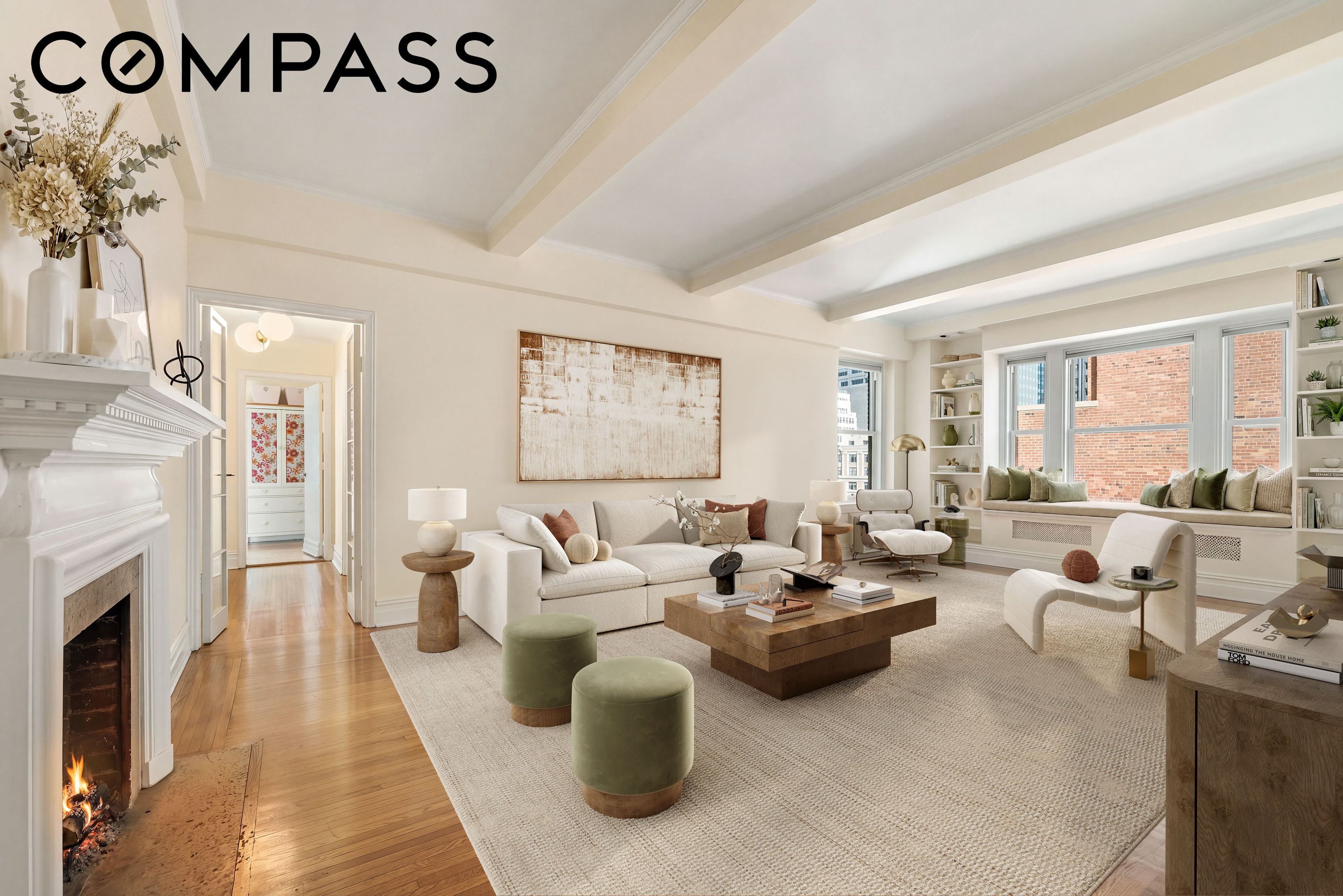 Staged living room with a lit fireplace, white sofa, and large windows overlooking neighboring buildings.