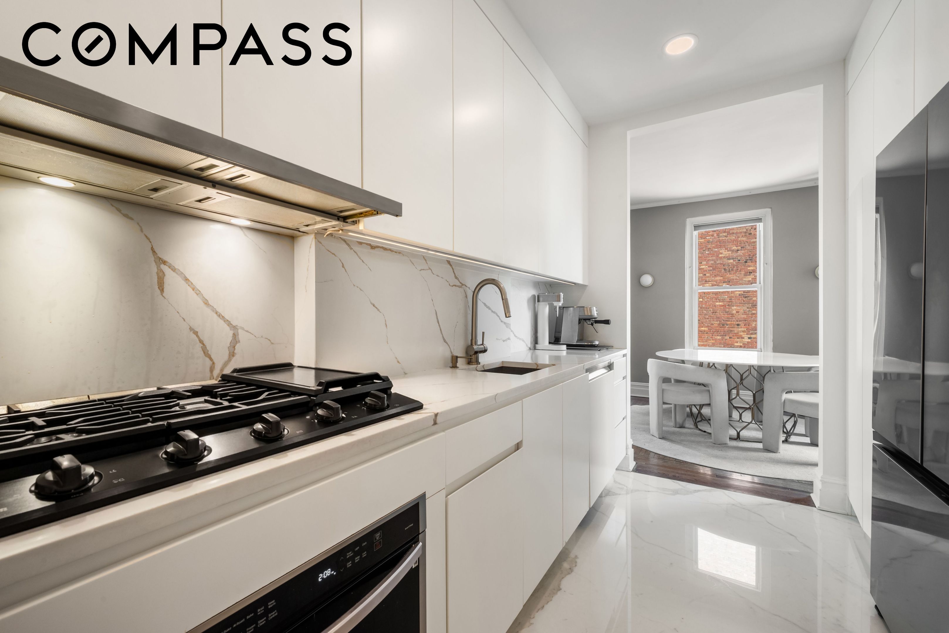 Modern white kitchen with marble counters, a gas range, and an adjoining dining nook.