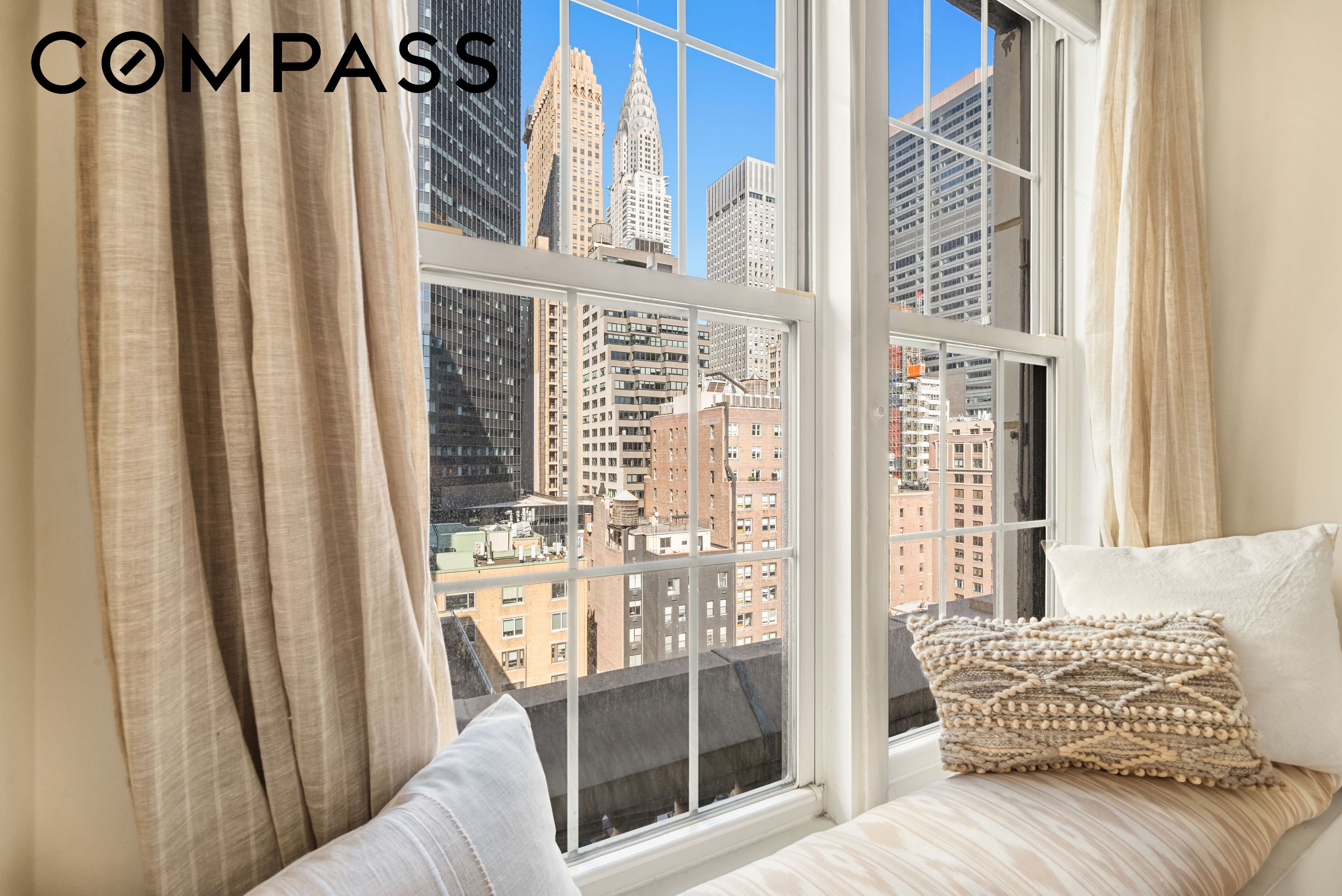Furnished window seat with beige curtains and a view of the Chrysler Building and Midtown skyscrapers.