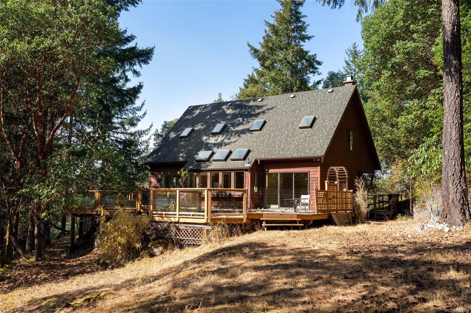 Wood-sided house with multiple roof skylights and a raised deck among tall trees.
