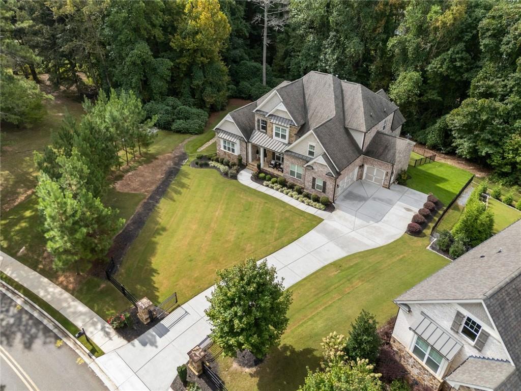 Aerial view of a two-story stone-and-siding house with a curved driveway and wooded surroundings.
