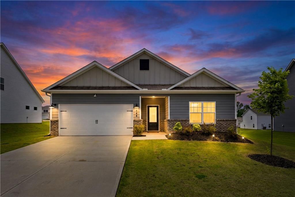 Gray single-story house with a two-car garage and brick accents beneath a colorful dusk sky.