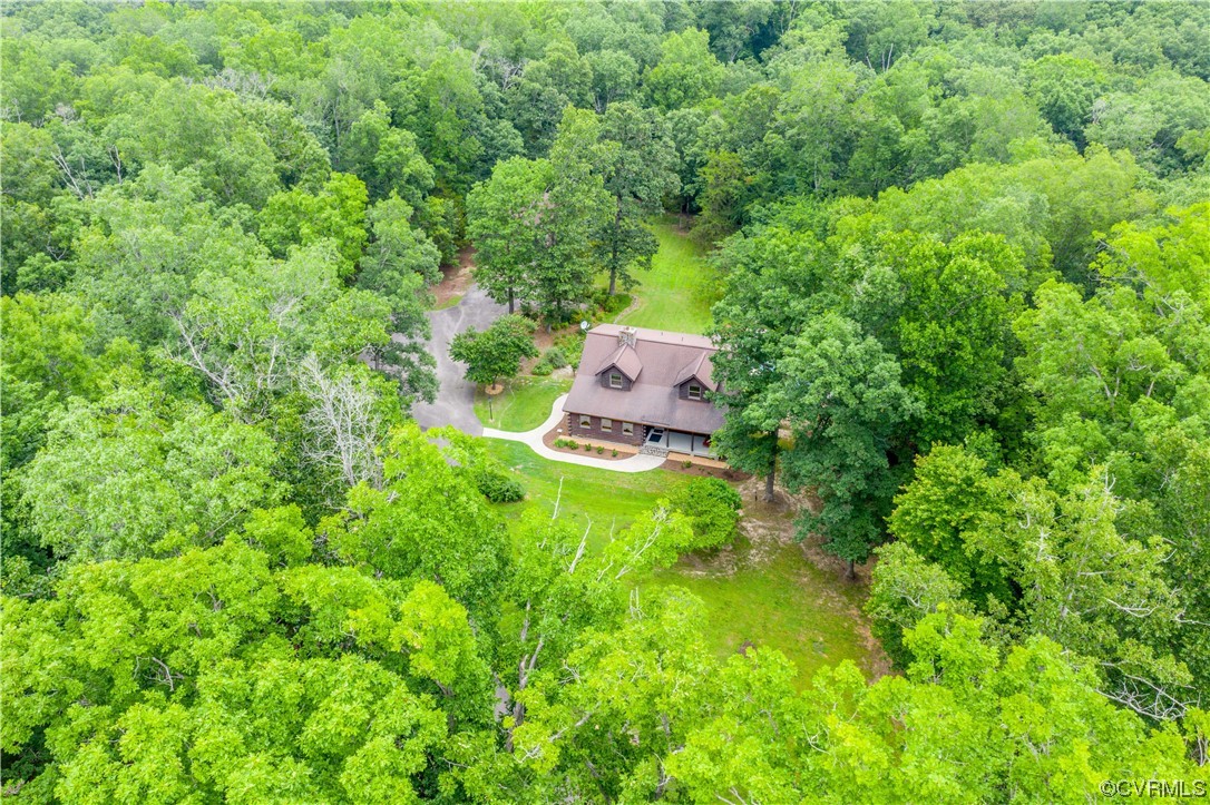 Aerial view of a house nestled among dense trees, with a lawn and curved driveway.