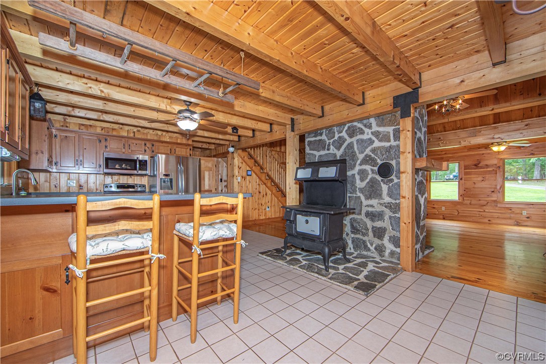 Rustic kitchen with timber beams, breakfast bar, and wood-burning stove against a stone wall.