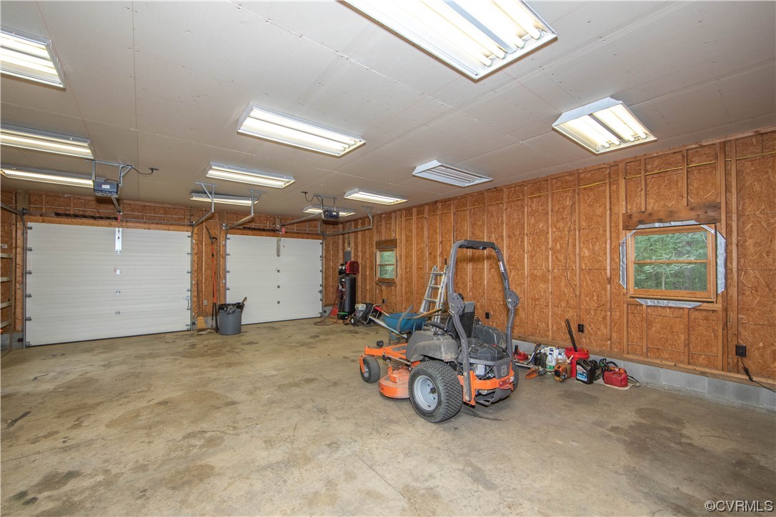 Two-car garage with unfinished wood walls, white overhead doors, and a riding mower.