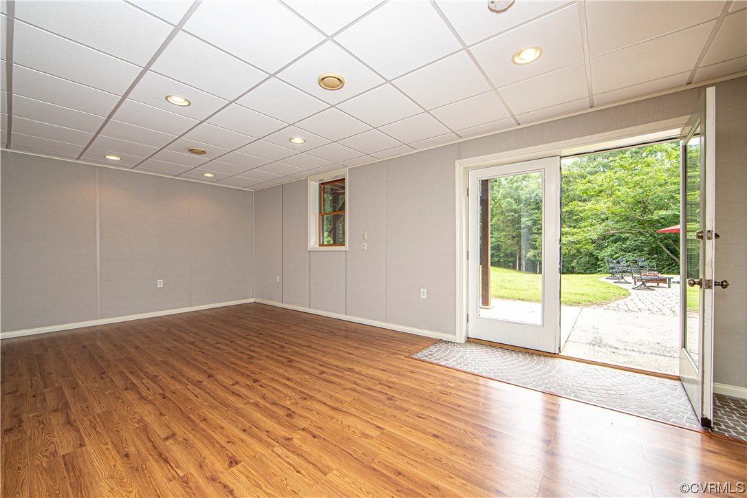 Empty finished room with wood-look floors and open doors to a patio and lawn.