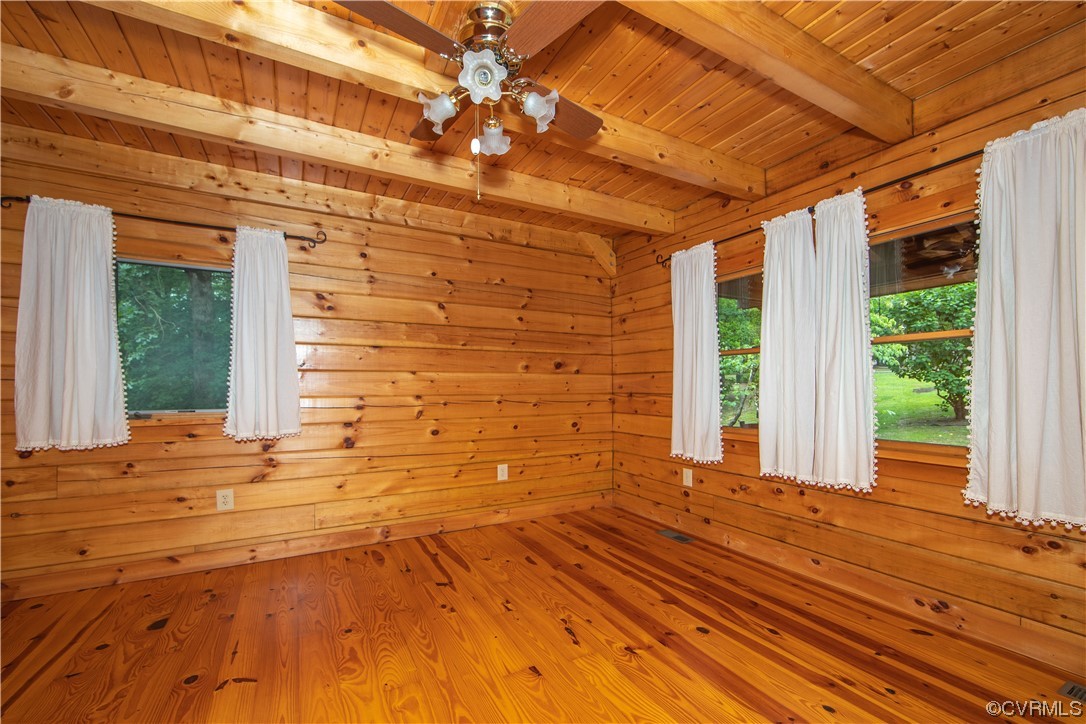 Unfurnished wood-paneled room with a vaulted ceiling, ceiling fan, and curtained windows.