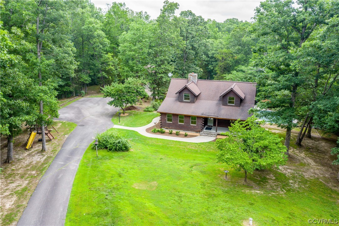 Aerial view of a wood-sided home surrounded by trees, lawn, and a curved driveway.