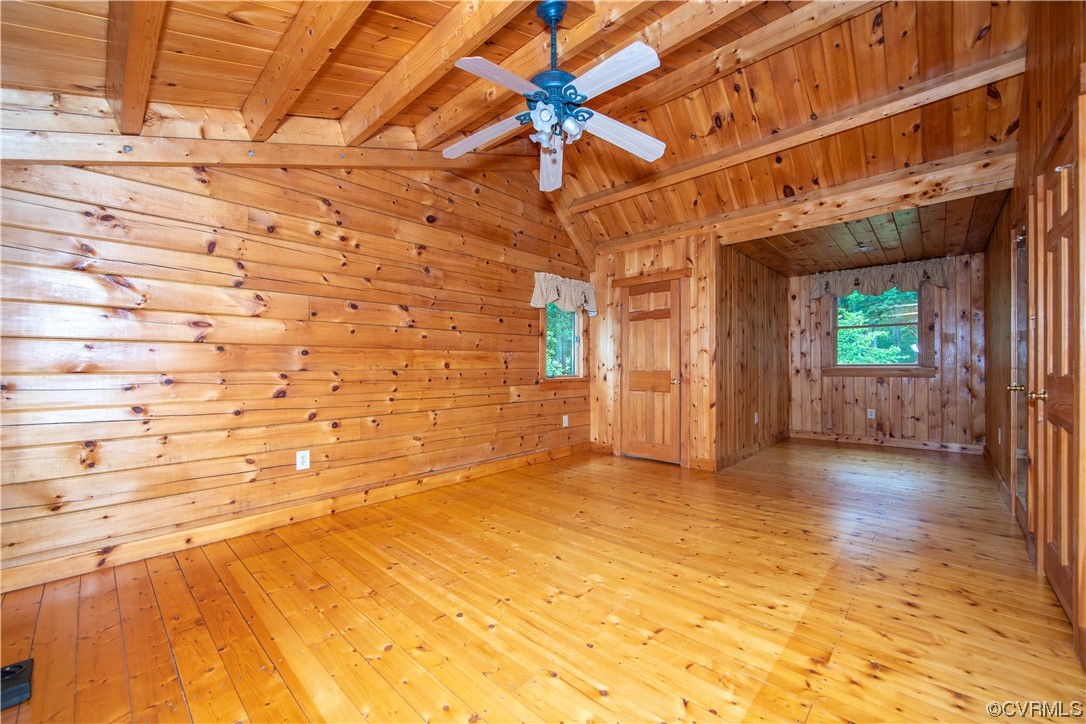 Vacant wood-paneled room with a vaulted ceiling, ceiling fan, and windows overlooking greenery.