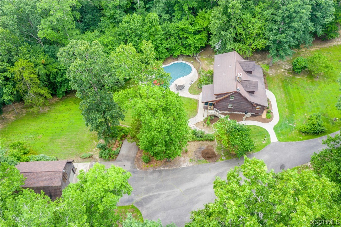Aerial view of a wooded home with a curved driveway and backyard swimming pool.