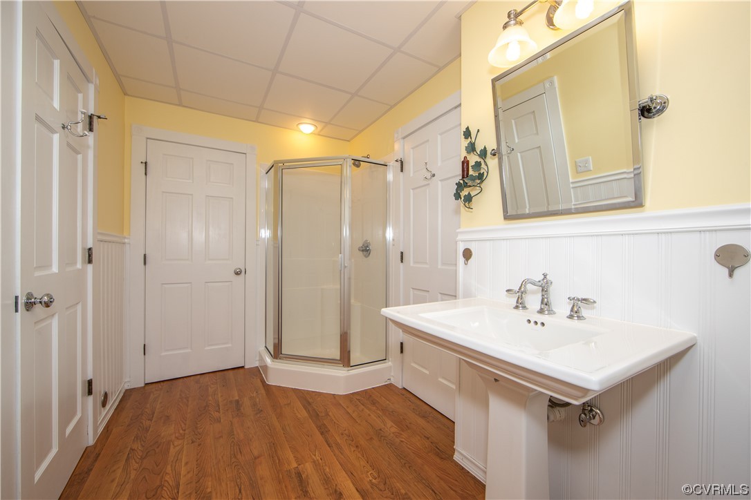 Bathroom with a glass corner shower, pedestal sink, and warm wood flooring.