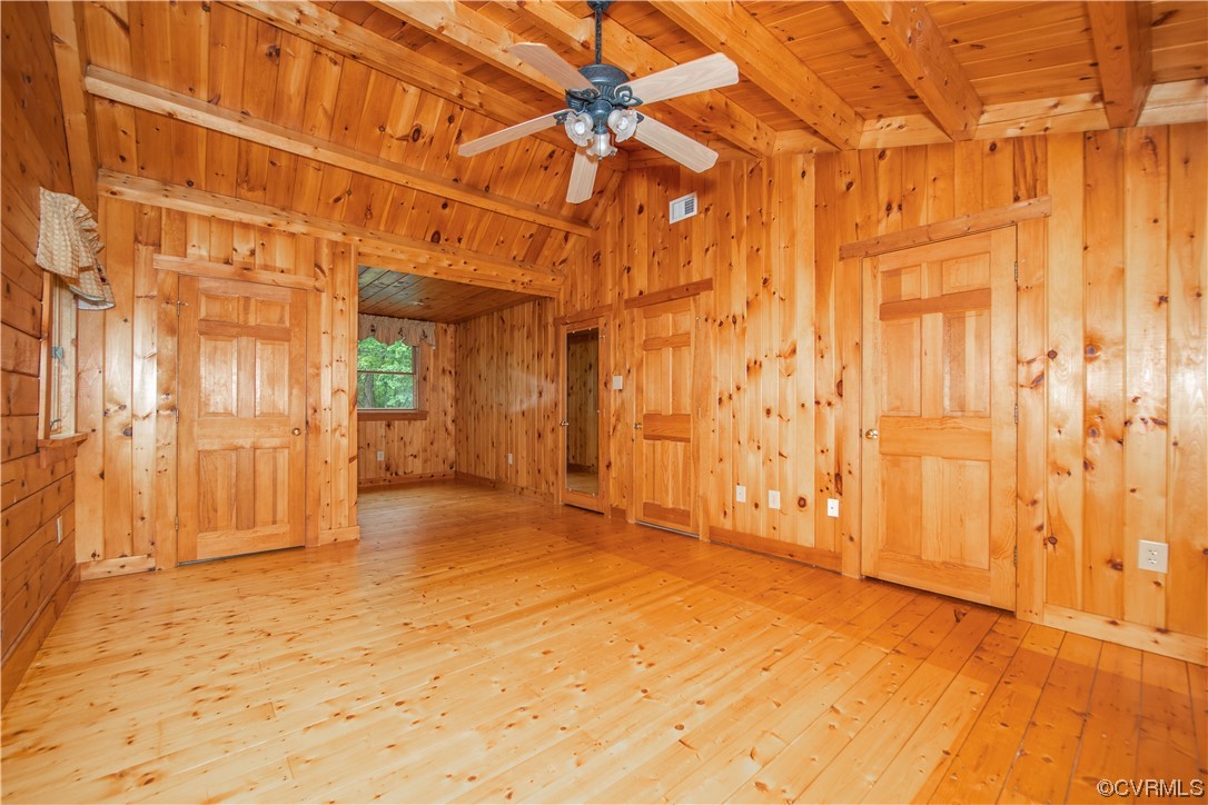 Vacant pine-paneled room with wood floors, a ceiling fan, and several wooden doors.