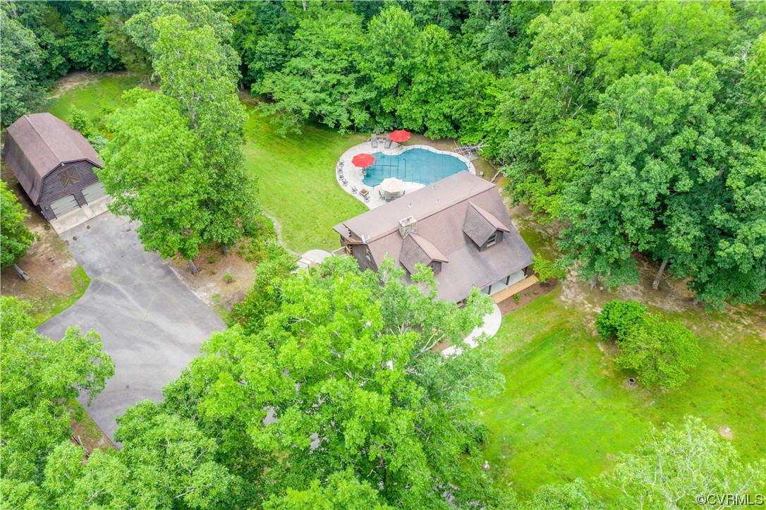 Aerial view of a wooded home with a swimming pool and detached outbuilding.