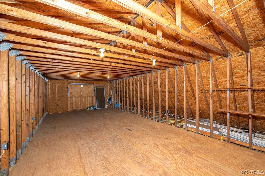 Unfinished attic with exposed wooden trusses, wall framing, and a broad plywood floor.