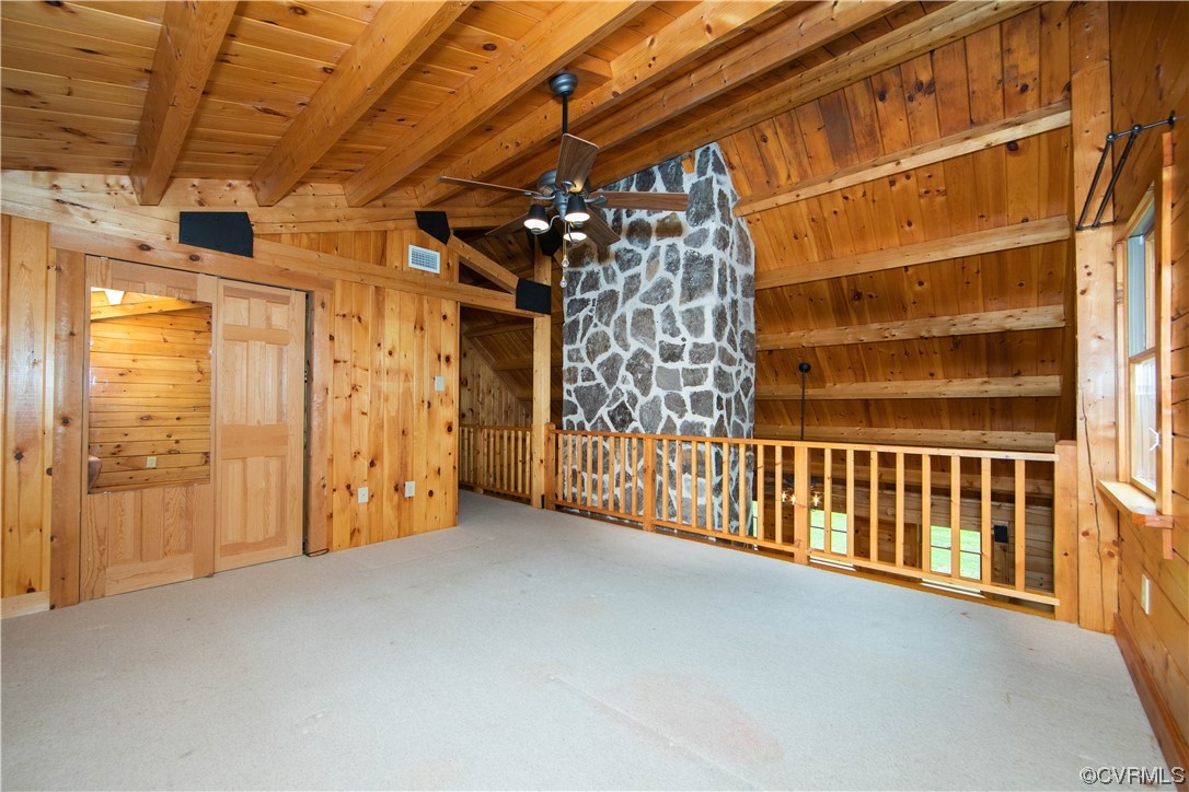 Carpeted loft with exposed wood beams, a wooden railing, and a tall stone chimney.