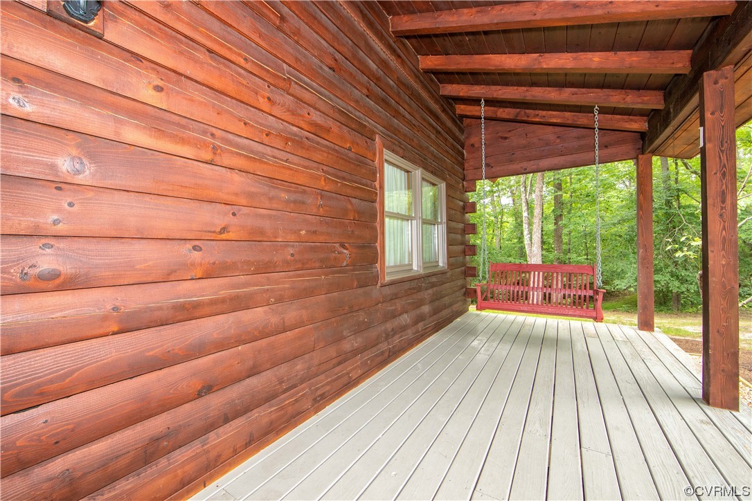 Covered log-sided porch with a red hanging bench overlooking leafy woods.