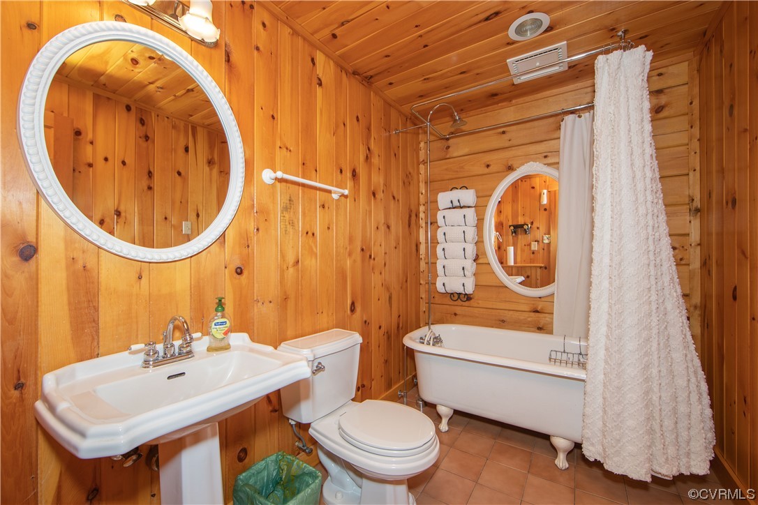 Wood-paneled bathroom with a white pedestal sink, clawfoot tub, and shower curtain.