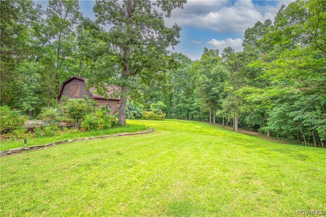 Wood-sided home partly screened by trees beside a broad green lawn and wooded grounds.