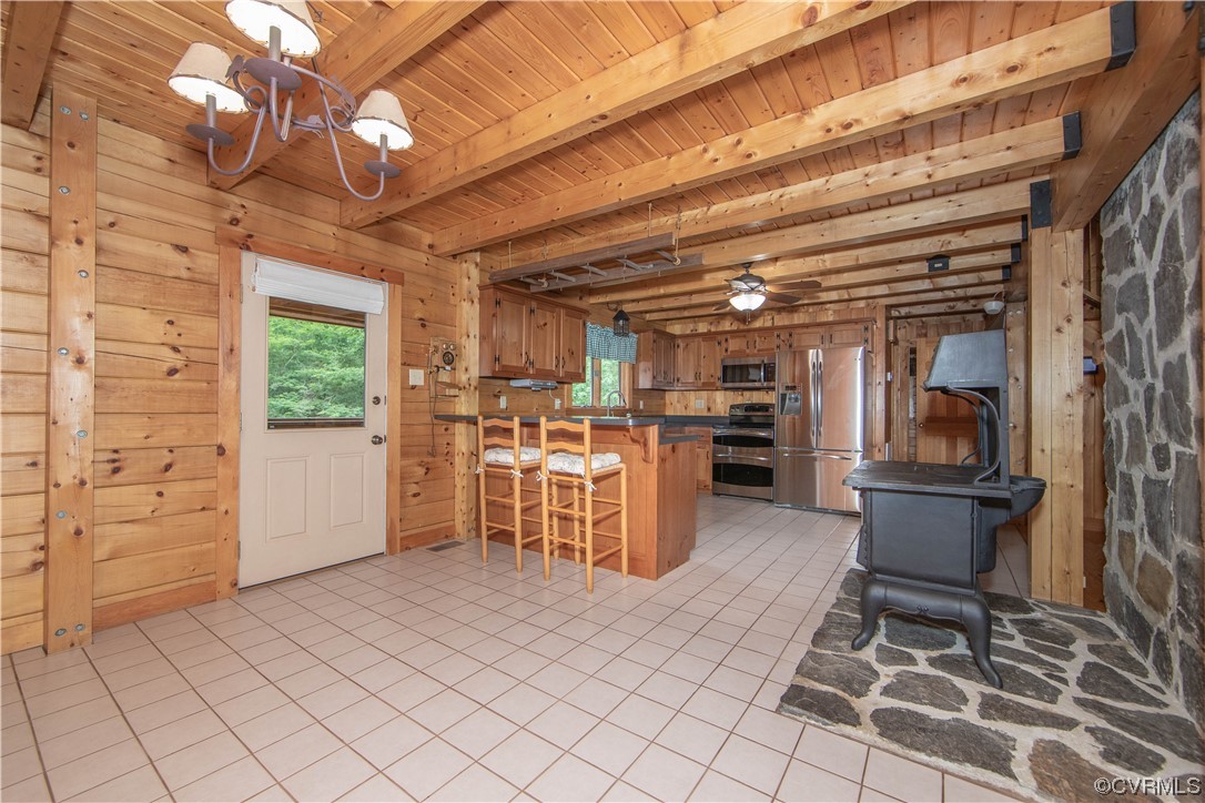 Rustic kitchen with knotty pine walls, exposed timber ceiling, stainless steel appliances, and a black wood stove.