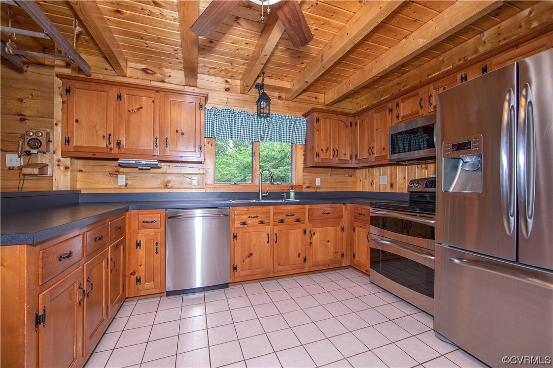 Wood-paneled kitchen with exposed ceiling beams, stainless appliances, and a window above the sink.