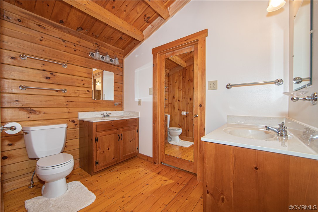 Bathroom with wood-paneled walls and vaulted ceiling, two vanities, and wood flooring.