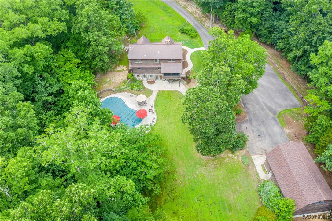 Aerial view of a wooded home with a curved pool, broad lawn, and long driveway.