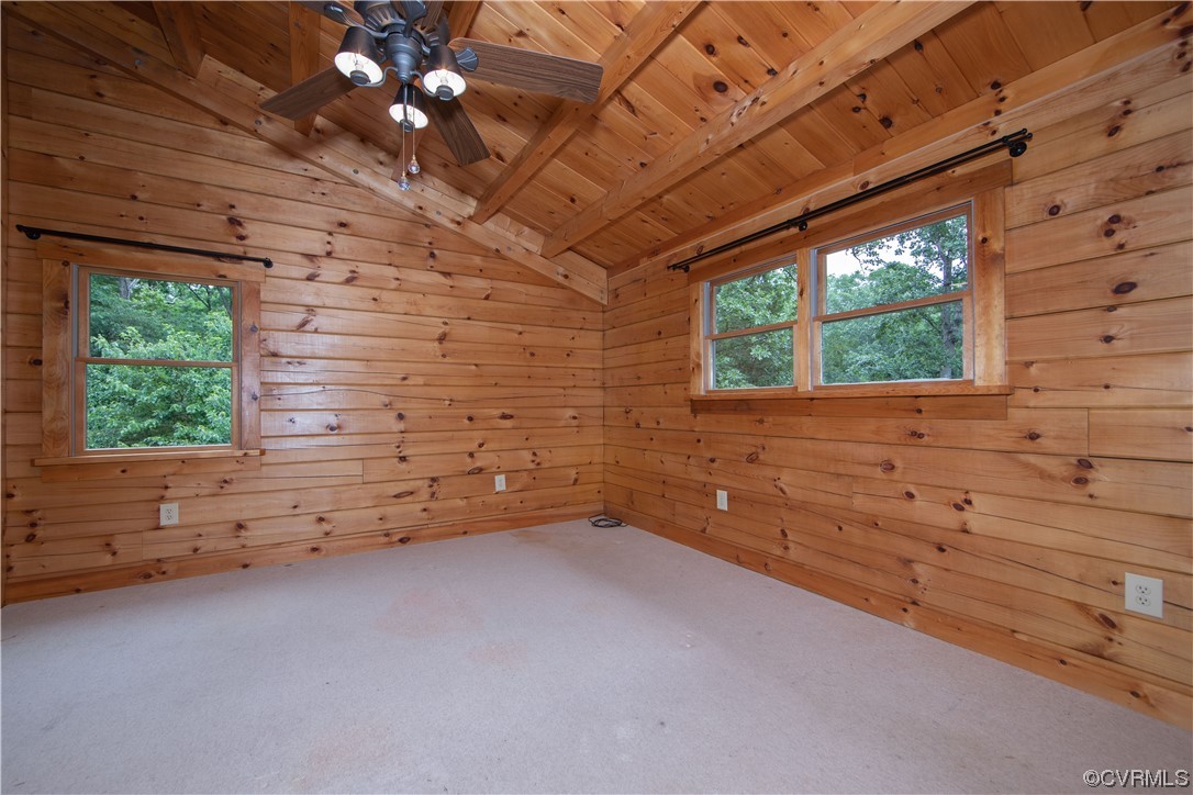 Empty pine-paneled room with a vaulted beam ceiling, ceiling fan, and windows overlooking trees.