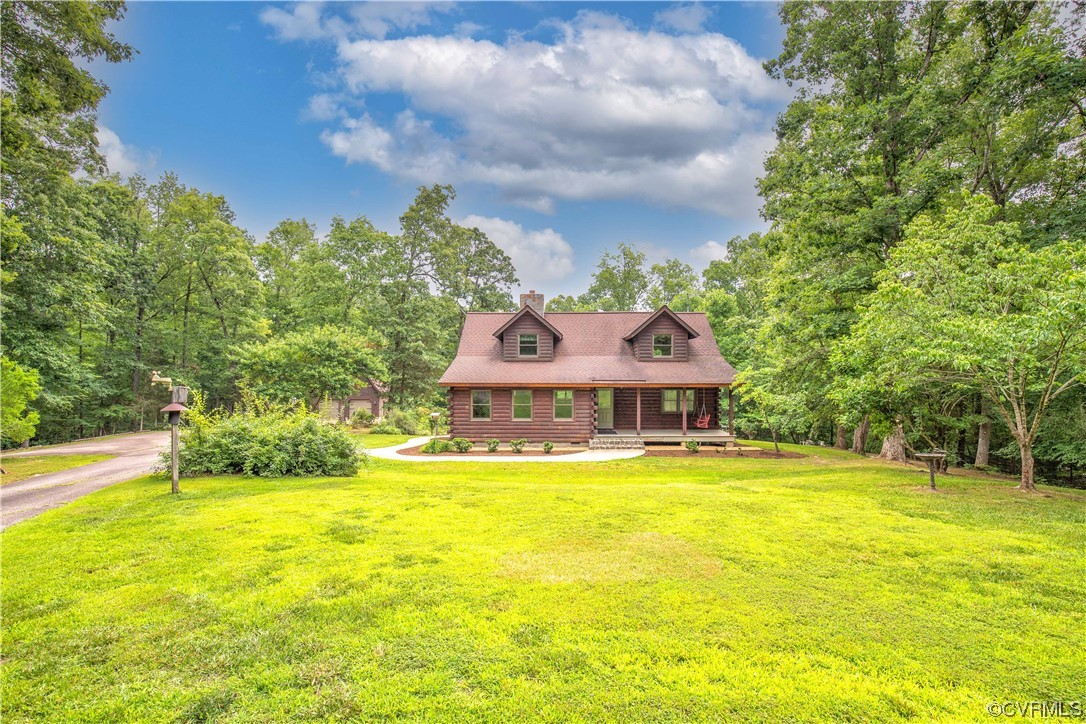Log cabin home with two dormers and a covered porch, surrounded by a broad lawn and mature trees.