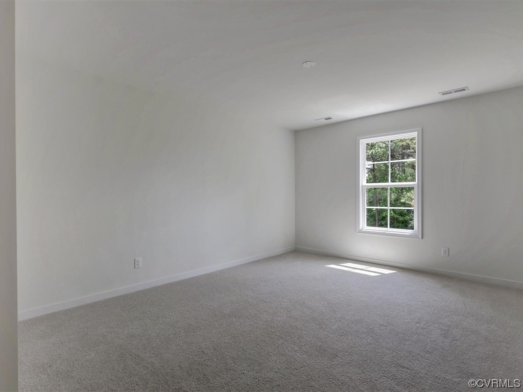 Empty carpeted room with gray walls and a window overlooking trees.