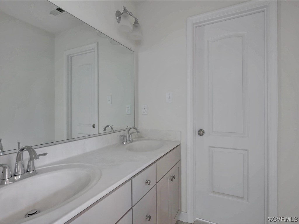 Bathroom vanity with two sinks, chrome faucets, a large mirror, and a white paneled door.