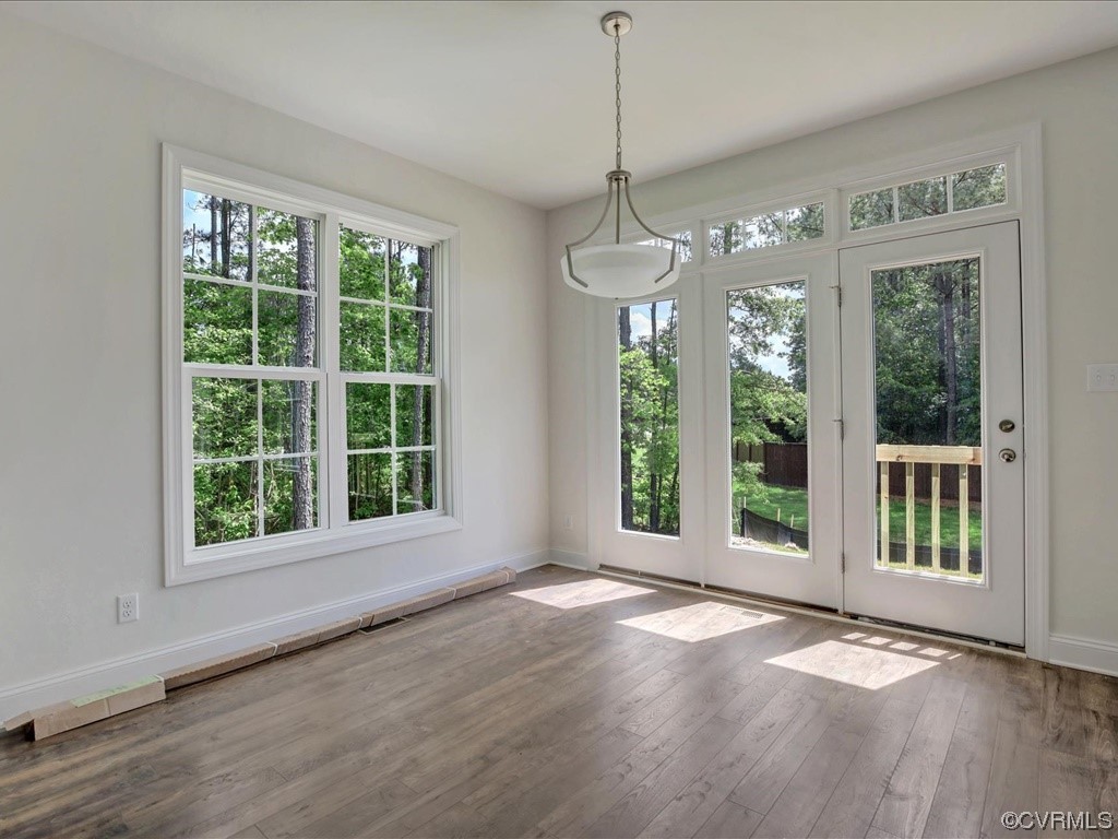 Empty room with gray wood-look floors, large windows, and a glass door facing a wooded backyard.