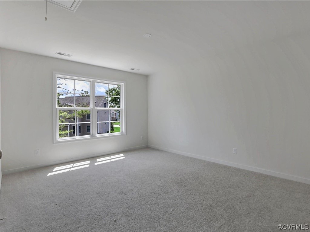 Empty carpeted room with white walls and a large window overlooking neighboring homes.