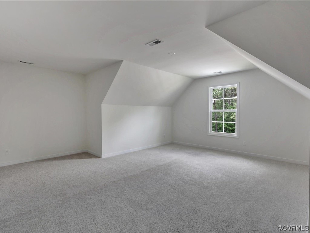 Empty finished attic room with gray carpet, sloped ceilings, and a window overlooking trees.