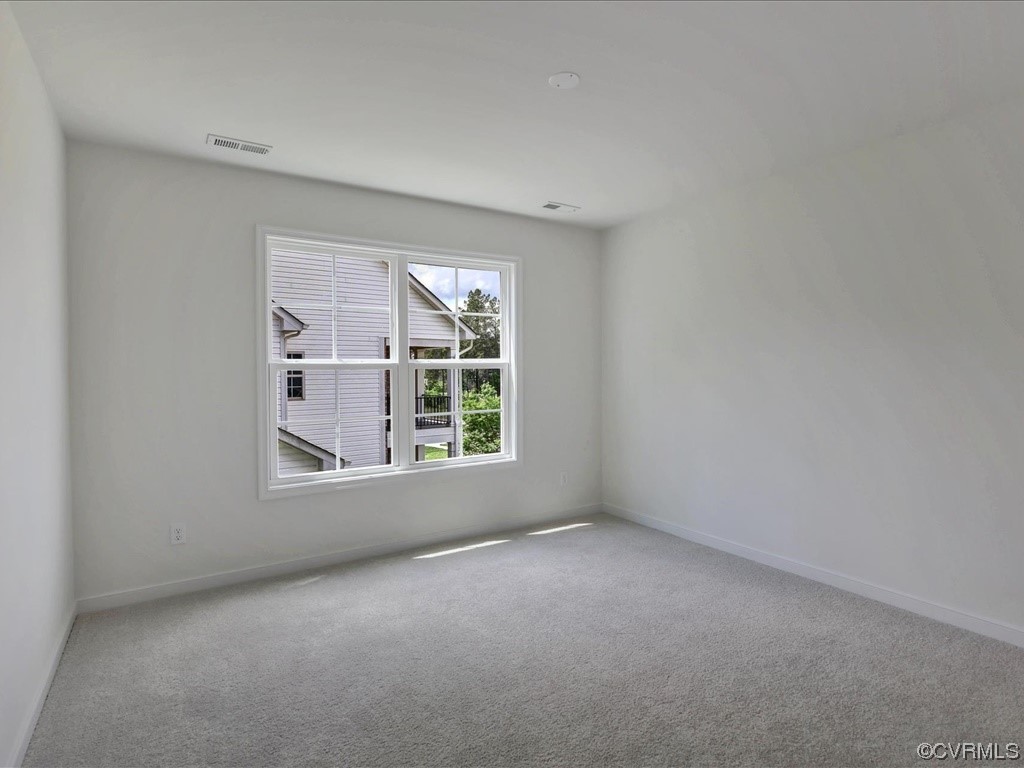 Empty carpeted room with a large window overlooking a neighboring house and greenery.