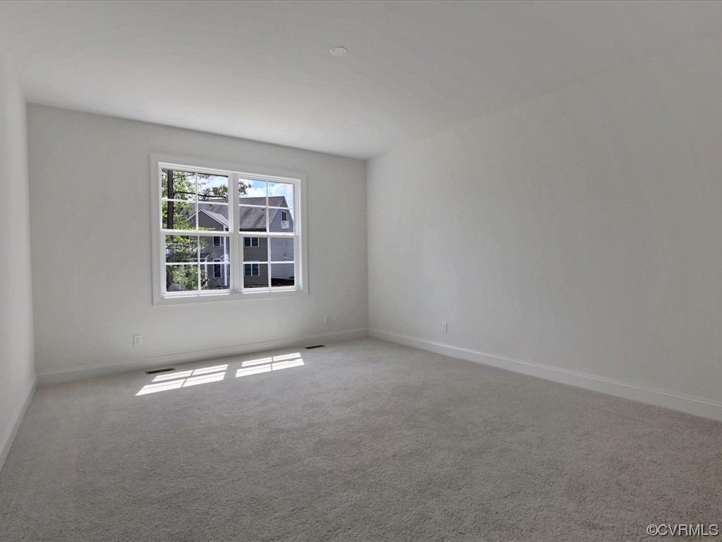 Vacant carpeted room with a large divided-pane window and sunlight across the floor.