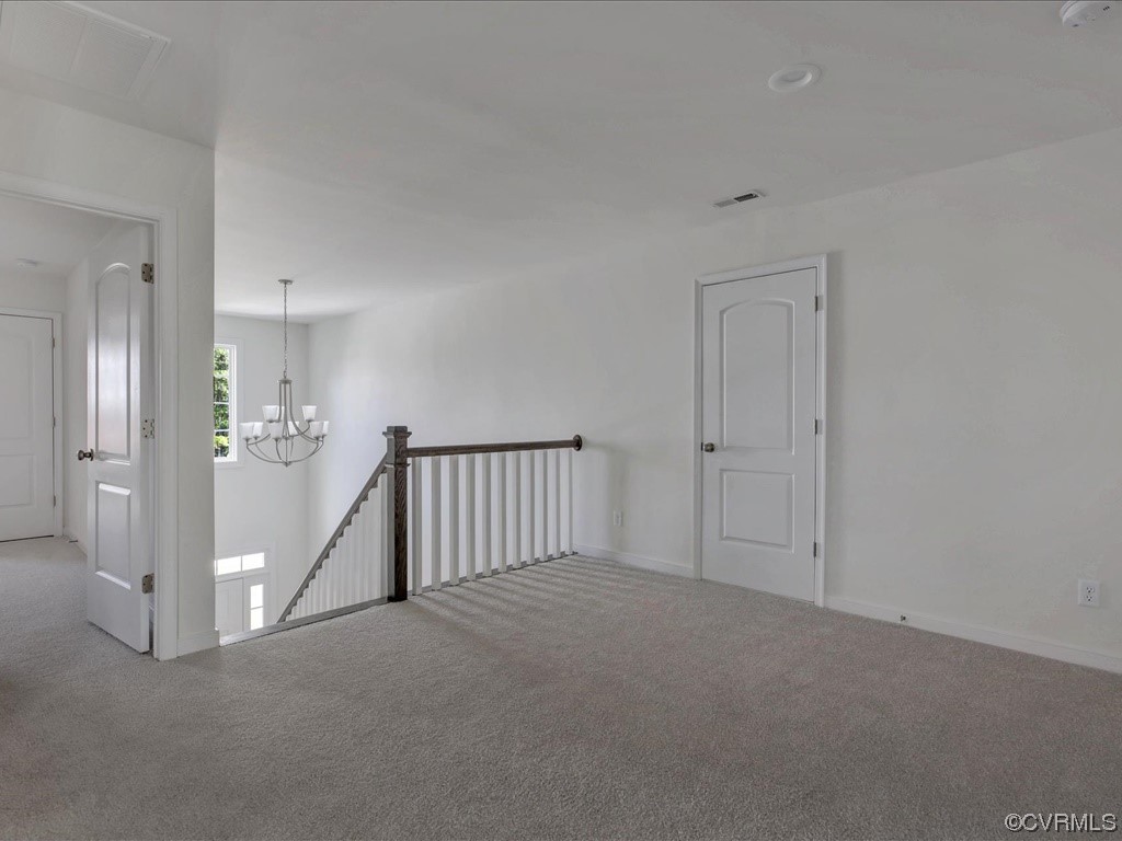 Upstairs landing with gray carpet, a dark wood stair railing, and a chandelier over the stairwell.