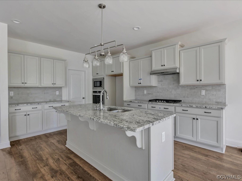 Kitchen with white cabinetry, a large stone-topped island, gray tile backsplash, and wood-look flooring.