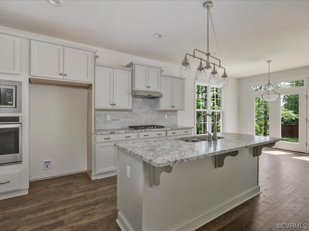Kitchen with a large stone island and white cabinetry, opening through glass doors to a wooded yard.