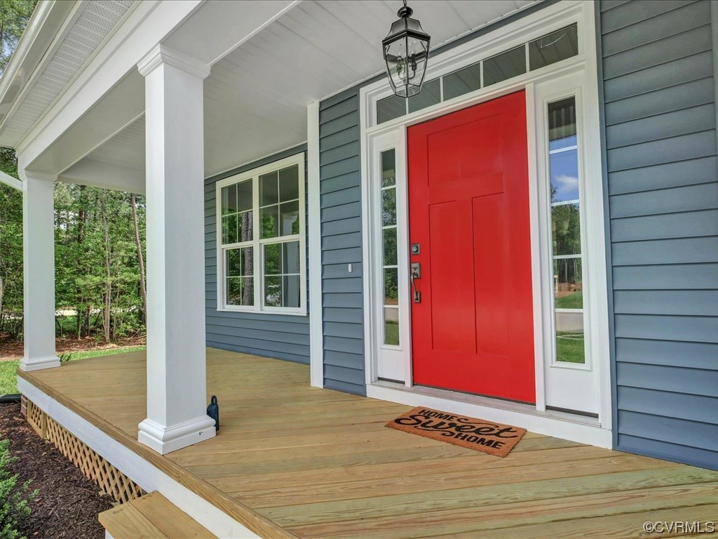 Home’s covered front porch with a bright red door, white columns, and wood decking.